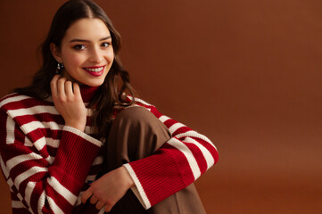 Fashionable happy smiling beautiful woman wearing red striped knitted turtleneck sweater,  posing on brown background. Close up studio fashion portrait. Copy, empty, blank space for text - 767177658
