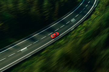 Dynamic Aerial View of a Vibrant Red Car Speeding Along a Serpentine Forest Road
