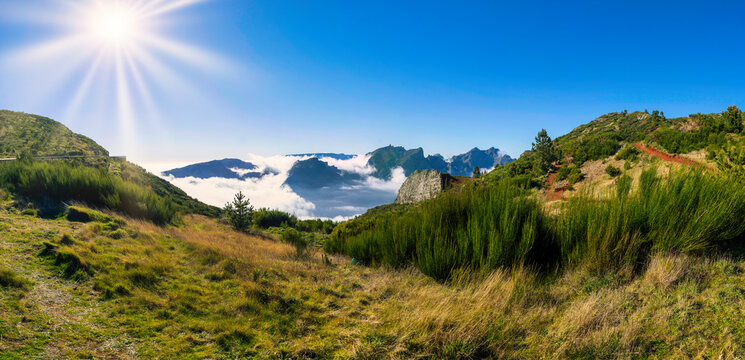 The photo portrays the Nuns Valley in Madeira, with green hills, rugged mountains, and a sea of clouds illuminated by the sun's rays, emphasizing its natural beauty and tranquil atmosphere.