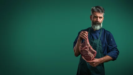 Foto op Canvas A mature chef with a distinctive beard poses with a significant raw steak on a refined dark backdrop © Fxquadro
