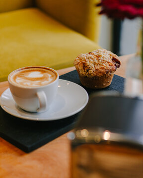 Latte and a chocolate muffin inside a city coffee shop and over a table with a yellow flower and beautiful interior design