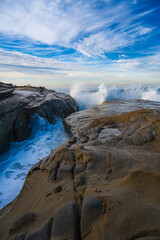 2022-01-14 WAVES CASHING ON THE ROCKS ALONG THE LA JOLLA SHORELINE WITH WATER SPRAYING AND A NICE BLUE SKY WITH NICE CLOUDS NEAR SAN DIEGO