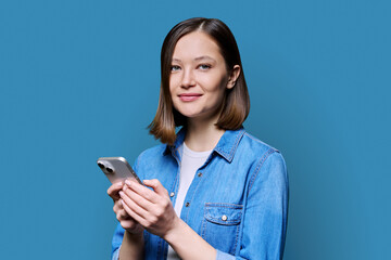 Young smiling woman using smartphone looking at camera in blue background