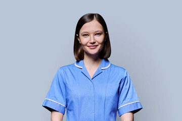 Portrait of young female nurse looking at camera on gray background