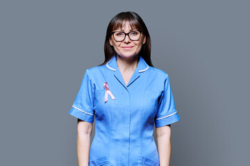 Smiling female nurse in blue uniform with pink ribbon, on grey background
