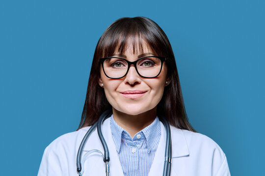 Headshot portrait smiling female doctor looking at camera on blue background