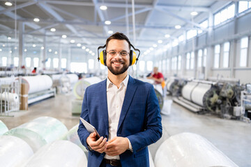 Portrait of successful caucasian manager in business suit standing in factory production hall.