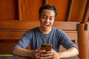 Man smile happy and surprised when looking at phone on the restaurant.