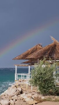 Slow motion colourful rainbow above the disquiet sea surface. Continuously changing weather conditions, light and shadow. Powerful waves crashing the coast after Storm Ciar&aacute;n smashed into Krk Island.