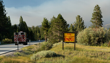 Fire restrictions sign in Sierra Nevada forest with fire truck passing by and smoky skies from...