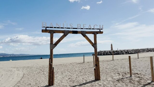 A rustic wooden sign marks the entrance to Banus Beach, inviting visitors to the sandy shore under a bright and sunny sky, Marbella, Spain, costa del sol
