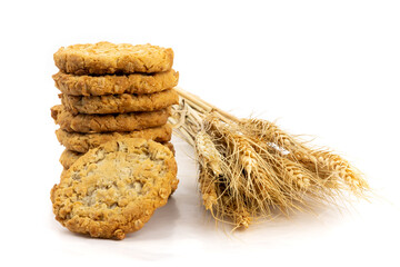 A stack of freshly baked oatmeal cookies with symbolic sheaf of oats, suggesting farm freshness, isolated on white

