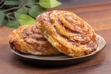 Large iced cinnamon buns, or danish butter horns, on a plate on a wooden table

