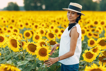 Beautiful young woman in a hat on a field of sunflowers - 767209628
