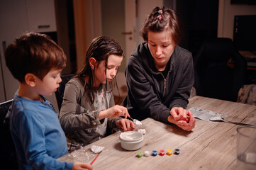 An absorbed group of siblings conduct a science experiment at home under the watchful eye of a young woman, fostering a collaborative and educational family moment