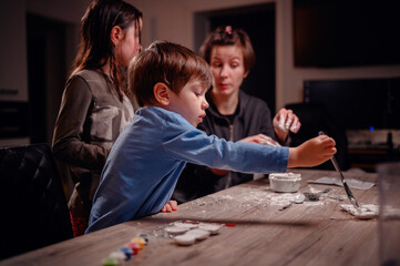 A young boy with a paintbrush, flanked by his family, deeply focused on painting, portraying a...