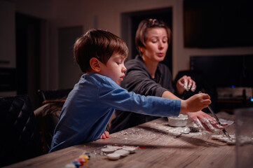 A boy paints with utmost concentration, with an adult nearby engaging in pottery, depicting a...
