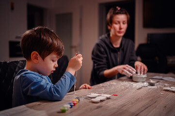 A boy paints with utmost concentration, with an adult nearby engaging in pottery, depicting a serene, domestic scene of individual creative pursuits