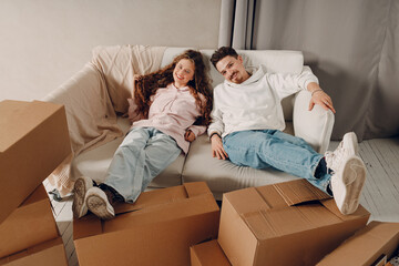 Happy young family couple man and woman relaxing on sofa after moving cardboard boxes to new estate home apartment. - 767210818