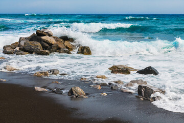 Santorini island, Greece. Waves on the Perissa beach with black volcanic sand.