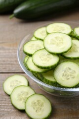 Cut cucumber in glass bowl on wooden table, closeup