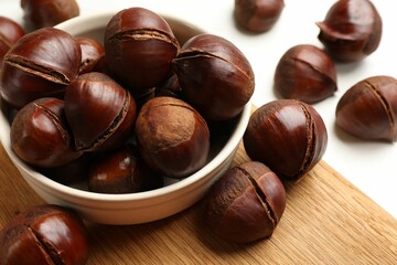 Bowl with roasted edible sweet chestnuts on white table, closeup