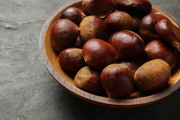 Roasted edible sweet chestnuts in bowl on grey textured table, closeup