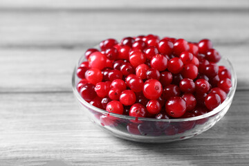 Fresh ripe cranberries in bowl on grey wooden table, closeup
