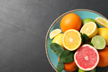 Different cut and whole citrus fruits on black table, top view. Space for text