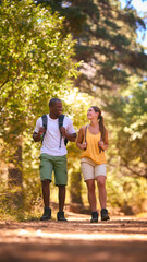 Young Active Couple Wearing Backpacks Hiking Along Trail Through Countryside