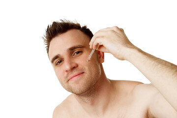 Young, handsome man with stubble looking at camera and applying serum against white studio...