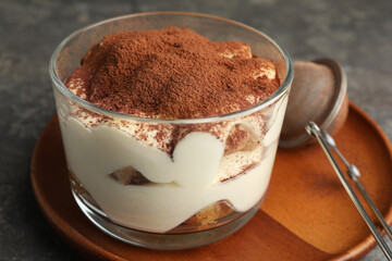 Delicious tiramisu in glass and sieve with cocoa powder on grey table, closeup