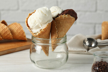 Ice cream scoops in wafer cones on white wooden table against brick wall
