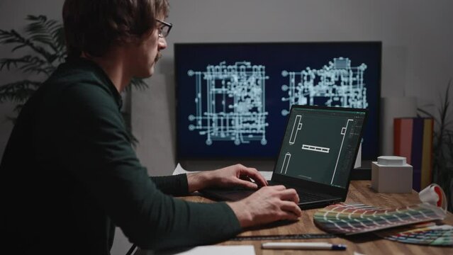 The video shows male hands working with a laptop. An architect is drawing a room project using CAD software. An unidentified male engineer is working in an architectural studio