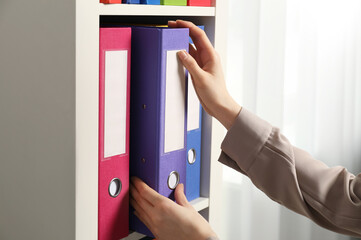 Woman taking binder office folder from shelving unit indoors, closeup