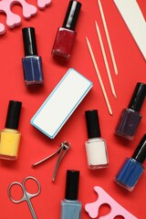 Nail polishes and set of pedicure tools on red background, flat lay