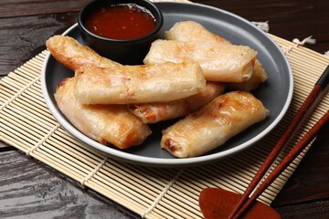Tasty fried spring rolls and sauce served on wooden table, closeup