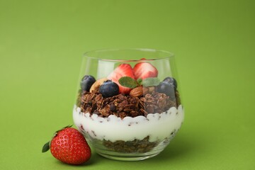 Tasty granola with berries, nuts and yogurt in glass on green background