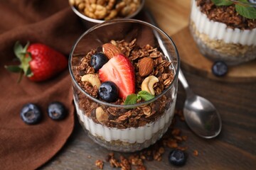 Tasty granola with berries, nuts and yogurt in glass on wooden table, closeup