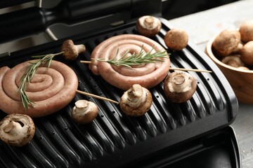 Electric grill with homemade sausages, rosemary and mushrooms on rustic wooden table, closeup