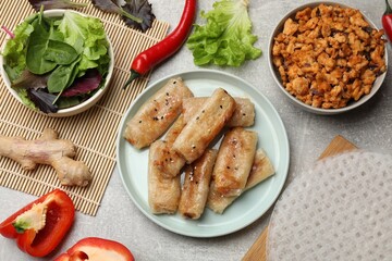 Tasty fried spring rolls and ingredients on grey table, flat lay