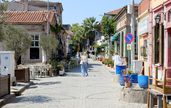 A sunny day on a cobblestone street in Cunda, Turkey, with pedestrians, cafes, and greenery. Cunda, Turkey - August 26, 2023