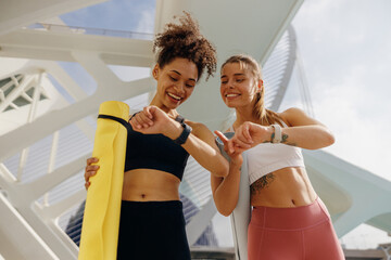 Smiling woman with female friend looking on smartwatch before exercising standing outdoors