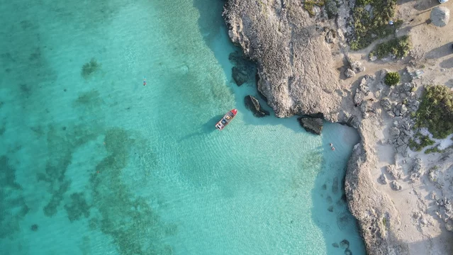 Aruba Tres Trapi snorkeling vertical areal photo of clear turquoise water with boat and rocky coastline