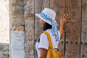 Beautiful woman with hat touching an ancient door at the entrance to ancient city of Rhodes on her...