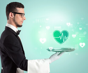 Handsome young waiter in tuxedo holding healthcare icons on tray - 767231455