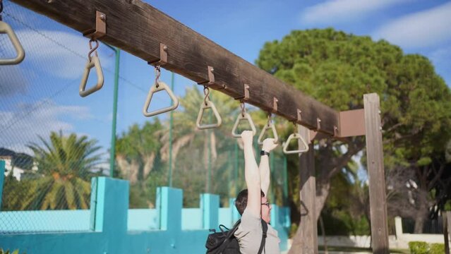 An individual trains on outdoor monkey bars, gripping the triangular rings with focus. The setup is in a park with lush trees in the background, promoting a healthy, active lifestyle.