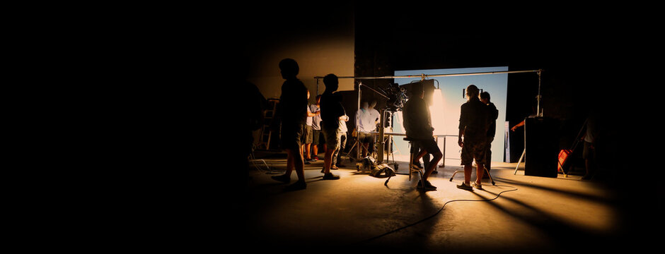 Silhouette images of video production behind the scenes of making of TV commercial movie shoot that film crew team lightman and camera man working together with director and equipment in big studio.