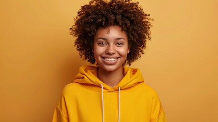 Obraz na płótnie Canvas Excited smiling happy student girl young woman with curly hair in hoodie on isolated yellow backgrou