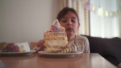 Happy young girl enjoying a large slice of decorative unicorn cake at her birthday party, with a joyful expression